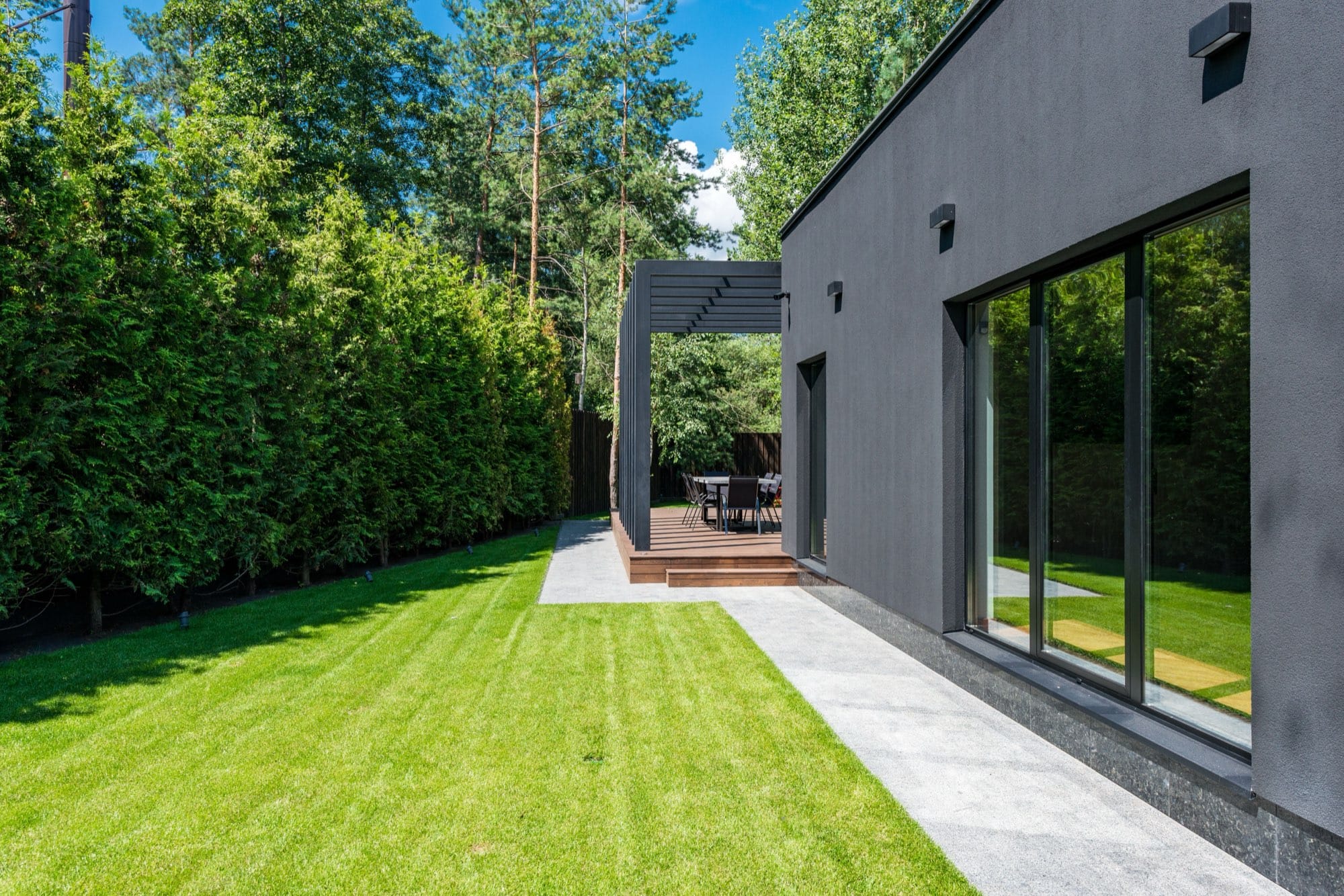 A modern home exterior with a freshly cut lawn, clipped hedges, and a pergola patio